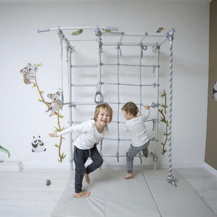 Two children playing on Swedish Giant Wallbars - S7 indoor climbing frame with rope ladder and rings.