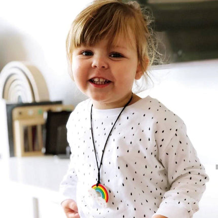 Young child smiling wearing a Rainbow Pendant necklace, promoting calm and sensory support for families.