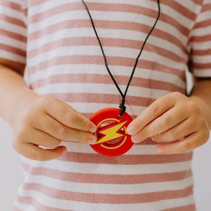 Child wearing striped shirt holding a red Strike Energy Pendant with yellow lightning bolt, sensory tool for calm support.