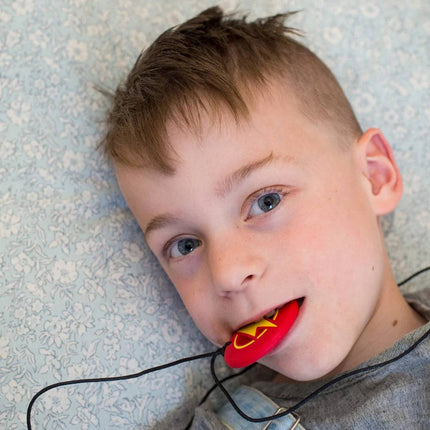 Child lying down holding a red Strike Energy Pendant in their mouth, helping families thrive with tools to calm.