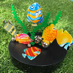 Magnetic Desk Sculptures - Colourful Fish balancing on metallic spheres with green seaweed on a black base outdoors on grass