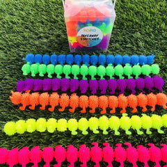 Rows of colorful textured stretch toys displayed on green grass beside a clear container