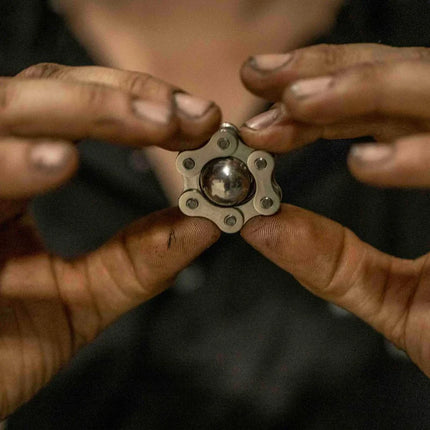 Hands holding a small metal sensory toy with a central ball and a star-shaped frame, Magic Ball Fidget by Kaiko