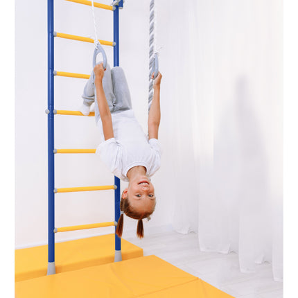 Child hanging upside down on rings attached to the Sensory Swedish Climbing Frame - No Drill with yellow mats beneath