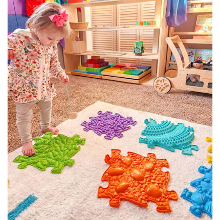 Child playing on colorful sensory mats arranged on carpet, featuring the Rainbow Tactile Floor mat Set