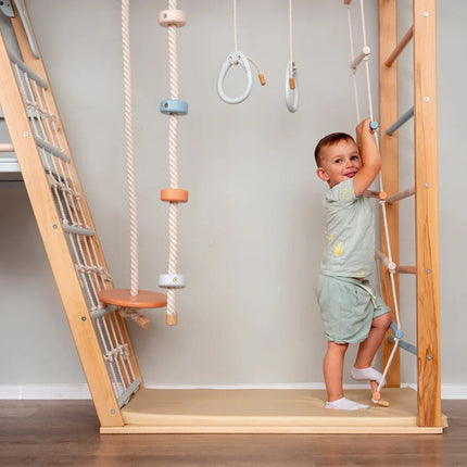 Child happily climbing wooden ladder on a Wooden Teepee Playground with ropes and gymnastic rings