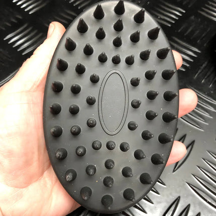 Hand holding a Black Tactile Sensory Brush with raised rounded and pointed nubs on black background.