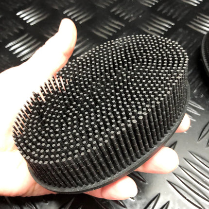 Hand holding a Black Tactile Sensory Brush with numerous soft bristles on a textured surface background