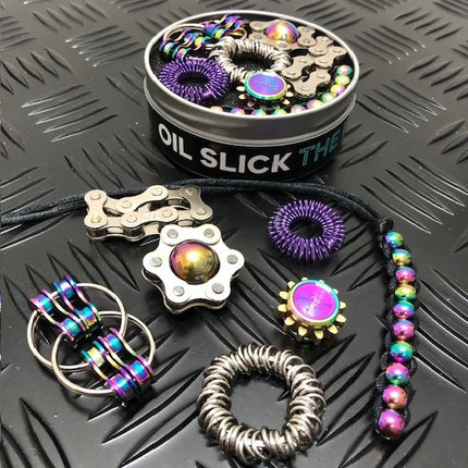 The Works Fidget Kit with metallic oil slick sensory toys arranged on textured black surface next to round storage tin