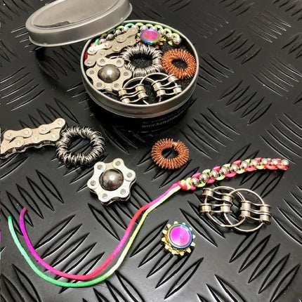 The Works Fidget Kit with metal rings, colorful braided strings, and textured sensory fidget tools in a small tin container.