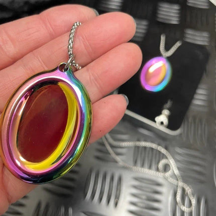 Hand holding a colorful metallic pendant from the Groove Stone - Dual Support Necklace & Key Chain with chain background.
